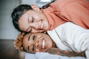 Imager of two women of color laying on top of each other smiling at the camera. Representing two women who could benefit from therapy for BIPOC. Where a BIPOC therapist can support your cultural diversity in counseling in North Carolina.
