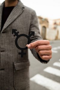 Image of a person in a coat holding a gender symbol representing all genders. Representing the support you can get in transgender affirming therapy with a LGBTQIA+ therapist in North Carolina. You can explore your identity and get support in coming out with LGBTQIA therapy in Chapel Hill, North Carolina.