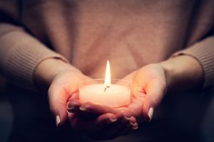 Image of a woman holding a single lit candle. Representing the symptoms that can be addressed in online therapy for grief in North Carolina. Whether you are in Durham, Raleigh, or anywhere else in North carolina you can feel better after loss with grief counseling.