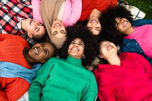 Photo of a group of diverse individuals laying together in a circle on the ground smiling. Looking for a diverse and culturally competent therapist? Start receiving support from a Be BOLD therapist with online therapy in North Carolina.